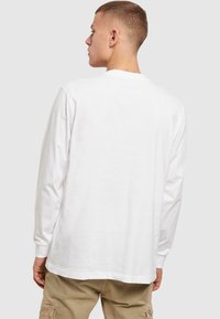 T-shirt bianco a maniche lunghe con scollo rotondo, design semplice e vestibilità rilassata. Materiale in morbido cotone, con polsini visibili sulle braccia.