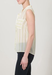 Blusa senza maniche in tessuto trasparente con righe verticali gialle e bianche, colletto e una tasca sul petto.