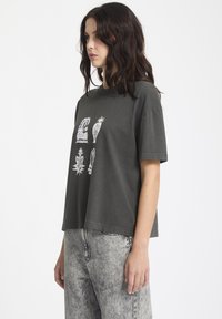 Camiseta de algodón gris oscuro de manga corta, con diseños gráficos en blanco de varias plantas en la parte delantera y un corte relajado.