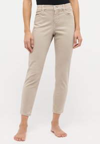 Pantalones de mezcla de algodón en color beige con corte ajustado, que presentan un cierre de botón y cremallera, pasadores para cinturón y bolsillos delanteros. Largo de tobillo sin dobladillo.