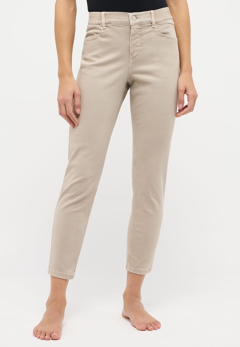 Pantalones de mezcla de algodón en color beige con corte ajustado, que presentan un cierre de botón y cremallera, pasadores para cinturón y bolsillos delanteros. Largo de tobillo sin dobladillo.