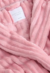 Lange roze pluche badjas met gestreept textuur en zacht materiaal. Etiket leest "NACHTKLEDING van NEXT." Heeft een sjaalkraag en een wikkelontwerp.