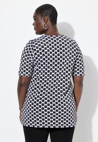 Top de patrón en blanco y negro con mangas cortas, que presenta un diseño geométrico y un escote redondo, combinado con pantalones negros.
