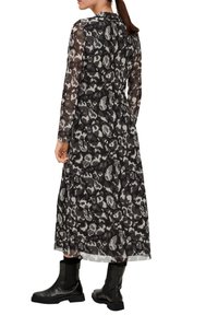 Langes schwarzes Kleid mit abstraktem grauem Tiermuster. Durchsichtige lange Ärmel und eine fließende Silhouette, kombiniert mit schwarzen Knöchelstiefeln.