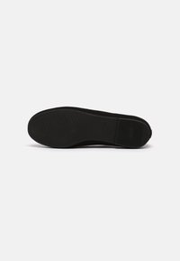 Semelle de chaussure noire avec des zones de grip texturées sur l’avant et le talon, présentée sur un fond clair uni.