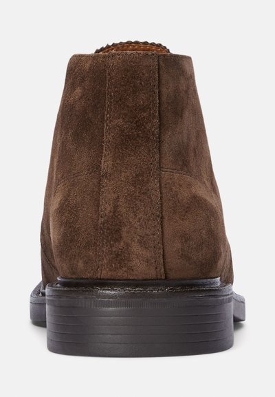 Botas de ante marrón hasta el tobillo con punta redondeada lisa y suela de goma negra, con detalles de costura en el talón y un diseño elegante.
