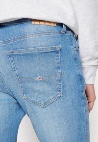 Jeans de mezclilla azul claro con una textura suave, que presentan una etiqueta de cuero marcada con "JEANS" y un único bolsillo trasero con un detalle de logo.