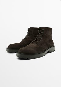 Stivaletti in suede marrone scuro con suola in gomma piatta, design con lacci e parte superiore leggermente testurizzata. Presentano una punta arrotondata e una costruzione robusta.
