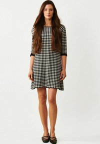 Mekko, jossa on mustavalkoinen ruudullinen kuvio, kolmannelta neljännekseltä hihat, levenevä helma ja mustat yksityiskohdat hihoissa. Yhdistetty mustien litteiden kenkien kanssa.