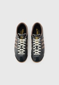 Sneaker in pelle nera con accenti marroni, lacci bianchi e tre strisce marroni. Presenta una punta testurizzata e una soletta imbottita.