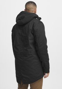 Svart parkajakke med hette, med et strømlinjeformet design, justerbar snøring og sidelommer med glidelås. Holdbart stoff med matt finish.