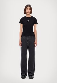 Svart bomullströja med en tight passform, korta ärmar och en vit logotyp. Kombinerad med hög midja och löst sittande mörk denim jeans.