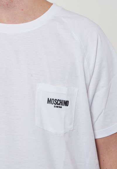 T-shirt bianco con maniche corte in un tessuto leggero, caratterizzato da una tasca sul petto sinistro con il logo nero "Moschino Swim". Texture liscia.