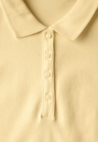 Ljust gult pikétröja med en texturerad krage, fem-knapps placket och slätt tyg. Enkelt mönster, inga mönster eller distinkta accenter.