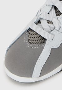 Šedá atletická bota s větrací mřížkou, hladkou syntetickou kůží a texturovanými akcenty. Obsahuje ploché šňůrky a zaoblený design špičky.