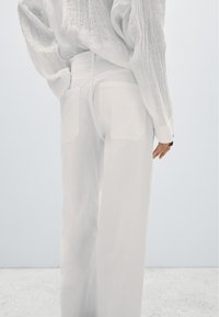 Vita vida byxor i slät tyg med två bakfickor, kombinerade med en vit texturerad långärmad skjorta.
