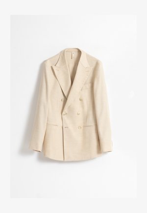 Blazer beige cruzado con solapas de muesca, dos bolsillos con solapa y cuatro botones en cada manga, mostrado sobre un fondo blanco.