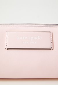 Vaaleanpunainen nahkalompakko, jossa on teksturoitu pinta, varustettuna vetoketjukiinnityksellä ja painettuna logo "kate spade NEW YORK" etupuolella.