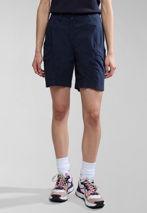 Pantaloni cargo blu realizzati in tessuto leggero, con chiusura a bottone, tasche curve e un taglio dritto. Indossati con scarpe da ginnastica colorate.