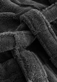 Grå, plyschfilt med en mjuk, texturerad yta och ett kors och tvärs-mönster. Tillverkad av ett fluffigt material för värme.