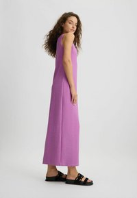 Lang, violet kjole med et enkelt design og en tætsiddende silhuette. Sammen med sorte sandaler med en sløjfe-accent.