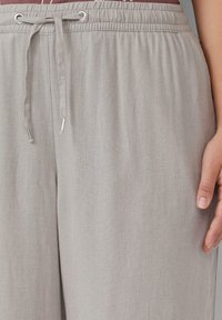 Lichtgrijze linnen broek met een elastische tailleband, verstelbaar trekkoord met metalen punten en een gladde, zachte textuur.