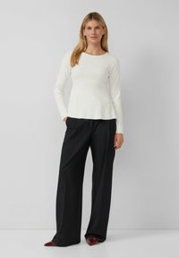 Haut à manches longues blanc à côtes avec un col rond, associé à un pantalon noir à jambes larges et des chaussures bordeaux à bout pointu. Texture lisse.