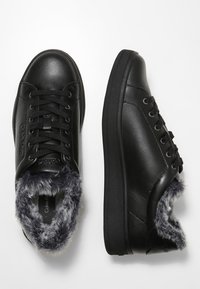 Baskets en cuir noir avec doublure en fourrure, semelle plate et bout arrondi. Dotées de lacets noirs, d'un logo et d'accents texturés sur le col.