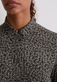 Black floral shirt featuring a button-up design with a pointed collar, soft fabric, and contrasting white floral patterns throughout.