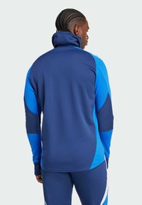 Blaues Sportjackett aus strukturiertem Stoff, mit Stehkragen und kontrastierenden Blautönen, sowie Paneeldetails und enganliegender Passform.