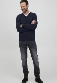 Marineblå V-hals genser i bomullsblanding, med hvit krage. Kombinert med mørkegrå jeans og svarte ankelstøvler. Uformell passform og rent design.