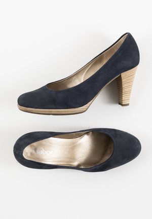 Zapatos de tacón alto de ante azul marino con punta redonda y tacón de madera beige texturizada. Cuenta con un interior acolchado dorado.