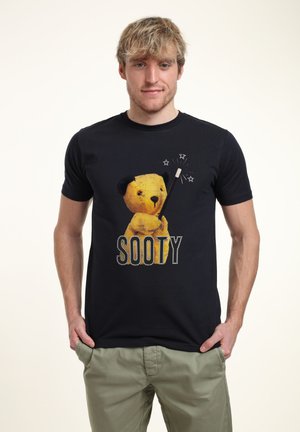Námořnické tričko s žlutou grafikou medvěda, který drží kouzelnou hůlku, a pod ním je slovo "SOOTY" napsané bílými tečkami. Vyrobeno z bavlny.