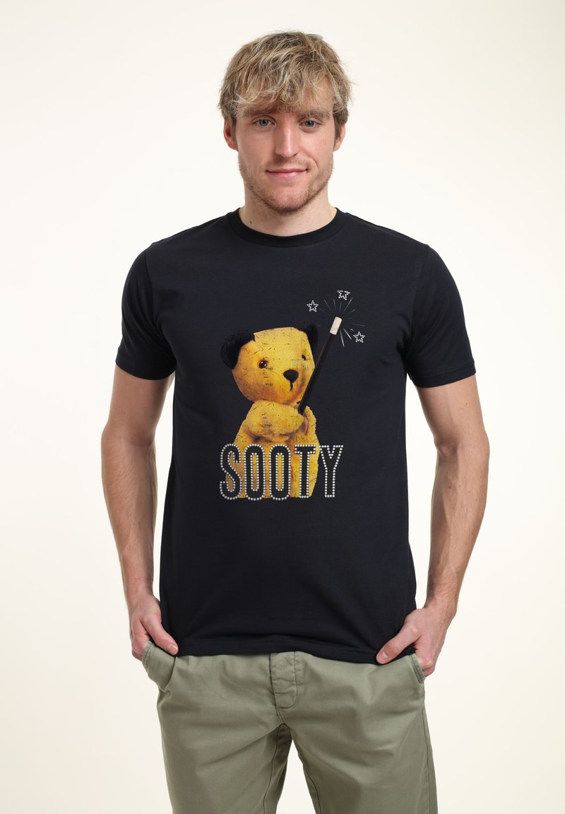 Navy T-shirt med en gul björn grafik som håller ett trollspö, med ordet "SOOTY" nedanför i vita prickar. Tillverkad av bomull.
