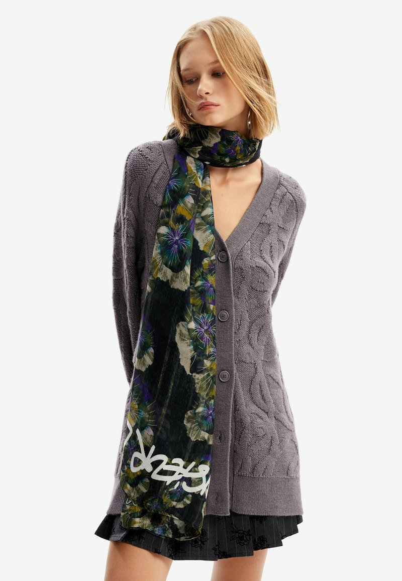 Cardigan grigio lavorato a maglia con scollatura a V profonda e bottoni, abbinato a una lunga sciarpa a fiori che presenta tonalità di verde, viola e nero.