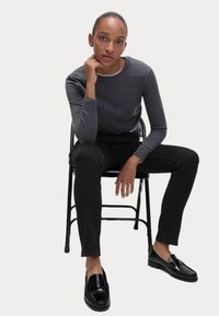 Szara koszula z długim rękawem i okrągłym dekoltem, w zestawieniu z dopasowanymi czarnymi spodniami i błyszczącymi czarnymi loafersami. Prosty design, gładka tekstura i klasyczne kolory.