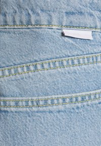 Tela de denim azul claro con costuras amarillas, que presenta una costura horizontal y una pequeña etiqueta blanca unida al borde.