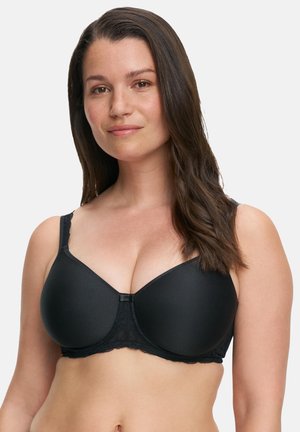 Woman with long brown hair wearing a black underwire bra, facing forward with a neutral expression and white background.