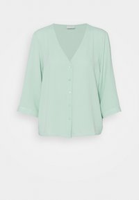 Blouse vert menthe avec un col en V et des manches trois-quarts. Dotée d'une patte de boutonnage à l'avant et d'un tissu lisse et léger.