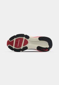 Semelle de chaussure présentant un design segmenté avec des pods de traction en caoutchouc noir, une semelle intermédiaire crème et des accents rouges sur le talon et le logo.