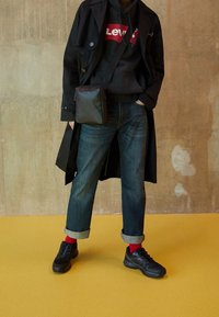 Abrigo negro sobre una sudadera gris con un logo rojo de Levi's, jeans azules con puños, calcetines rojos y zapatillas negras. Pequeño bolso negro cruzado.