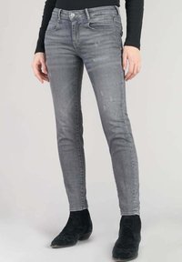 Jeans gris skinny avec une texture décolorée et un léger effet vieilli, dotés d'une fermeture à bouton à l'avant et de cinq poches, associés à des bottes noires.