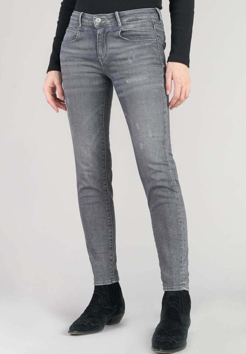 Jeans gris skinny avec une texture décolorée et un léger effet vieilli, dotés d'une fermeture à bouton à l'avant et de cinq poches, associés à des bottes noires.
