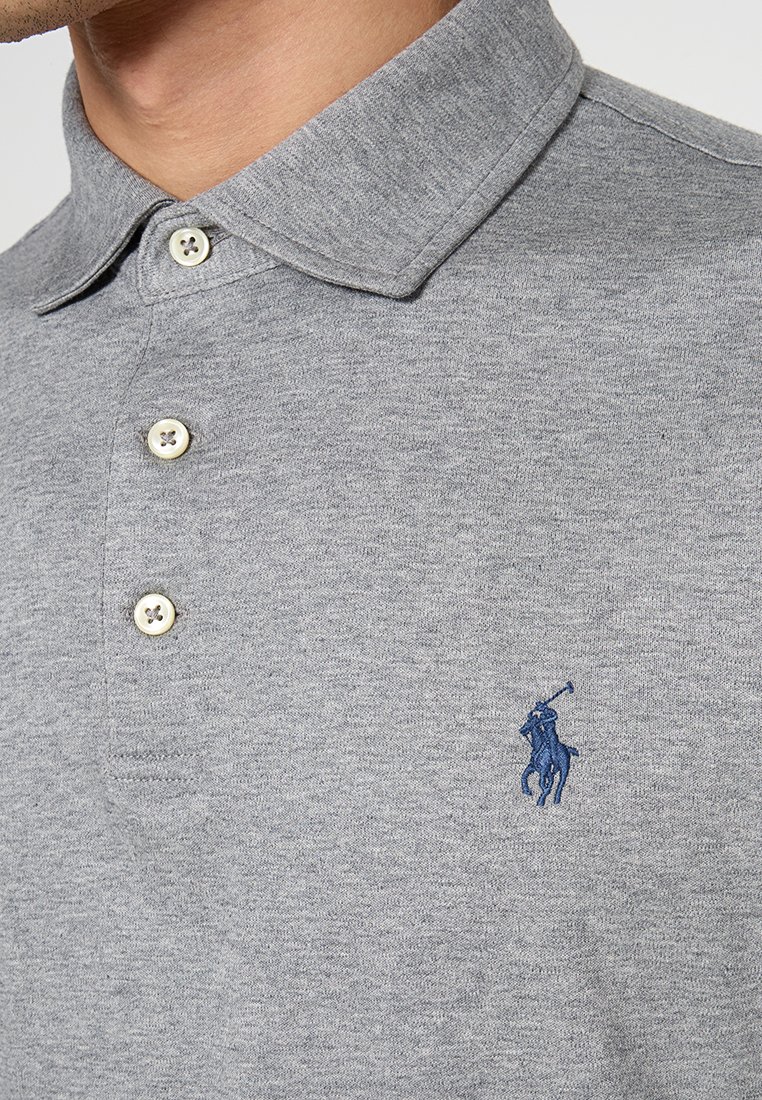 Polo gris hecho de una mezcla de algodón, con un cuello clásico, tres botones y un logo bordado en azul en el lado izquierdo del pecho.