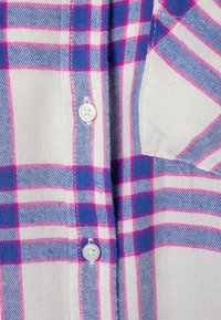 Camicia a scacchi con una combinazione di colori bianco, blu e rosa. Chiusura con bottoni e un'unica tasca sul petto, tessuto di cotone, texture liscia.