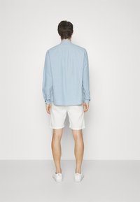 Jasnoniebieska koszula z długim rękawem, białe szorty i białe trampki. Koszula ma mankiety zapinane na guziki oraz detal w formie karczku z tyłu.