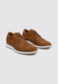 Zapatos de ante marrón con un diseño perforado, cierre de cordones, suela de goma blanca y un acento de cuero suave en el talón.