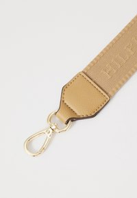 Sangle tissée beige avec une attache en cuir texturé, clip en matériel doré et lettrage en relief sur toute la longueur de la sangle.