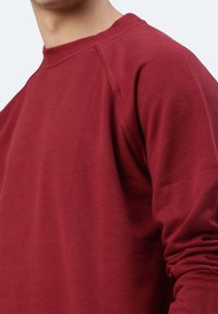 Felpa bordeaux con colletto tondo, maniche lunghe raglan e tessuto testurizzato. Presenta una vestibilità comoda e cuciture minime.