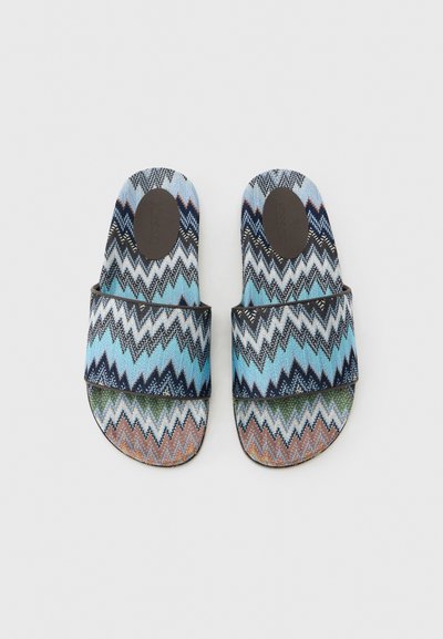 Paire de sandales à enfiler avec des brides larges en tissu à motif zigzag dans des tons de bleu, blanc, noir, vert et marron, au-dessus de semelles texturées.